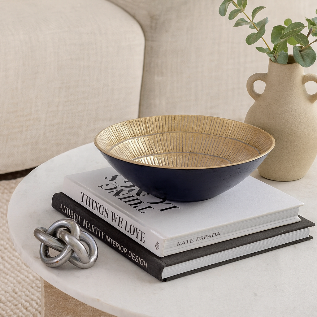 Black and gold decorative bowl styled on a marble coffee table with books, silver knot sculpture and ceramic vase – The Lighting Vault