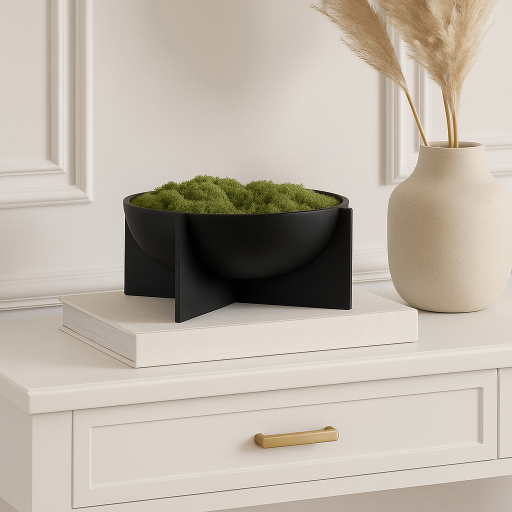 Black decorative bowl filled with layered green moss on stacked books and white console table