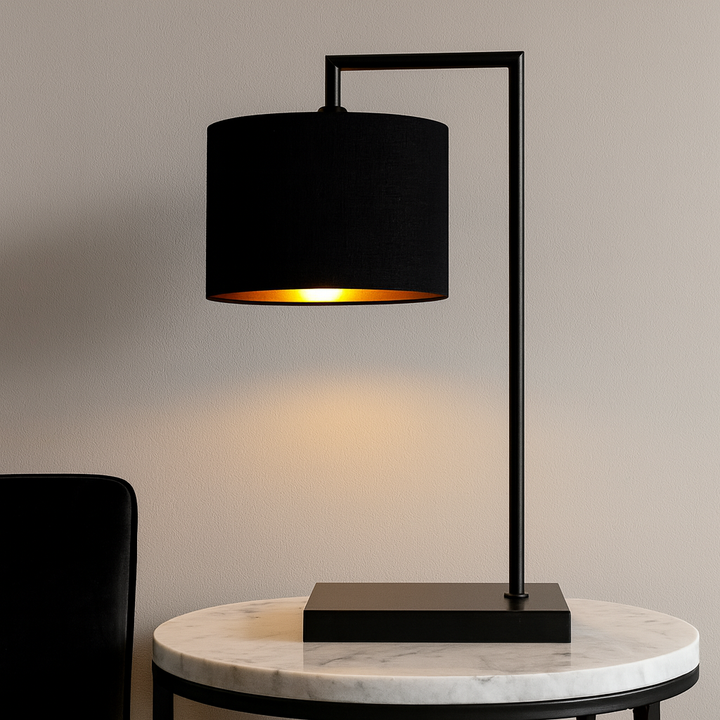 Luxury black table lamp with 25cm black shade and gold lining on a round marble side table against a neutral wall.