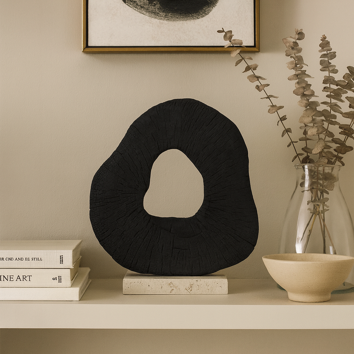 Luxury styled shelf with black organic ring sculpture on travertine base, paired with books, vase, and artwork.