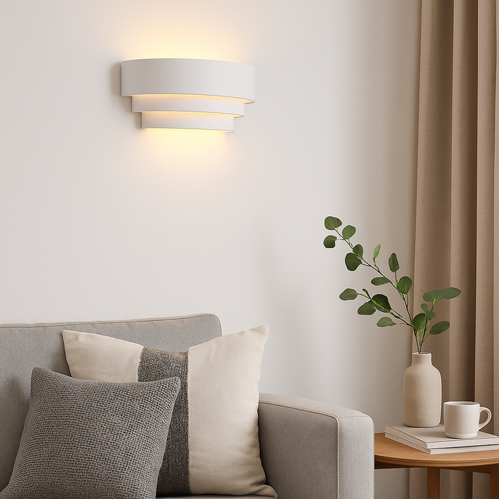 Borden white wall light in a modern living room, 31cm wide, casting warm glow above a sofa with cushions and side table styling