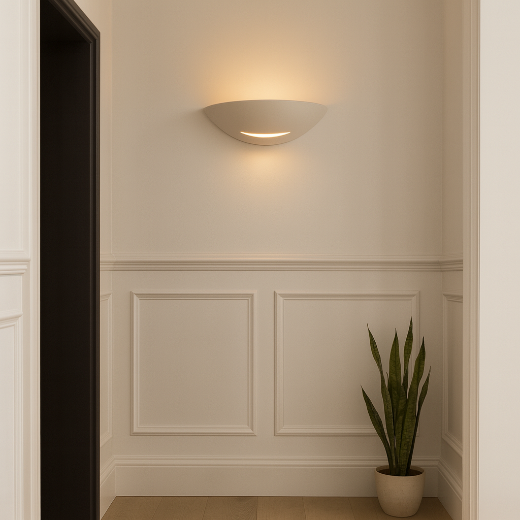 Brighton white ceramic wall light with warm glow in a modern hallway with white panelled walls, black door frame and potted plant