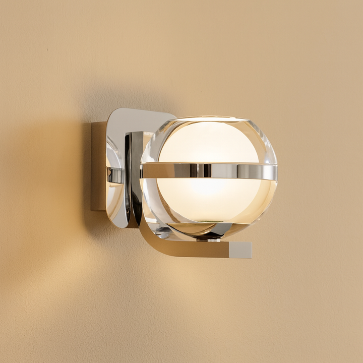 Modern chrome wall light with clear glass globe and frosted center casting a warm glow on a neutral wall