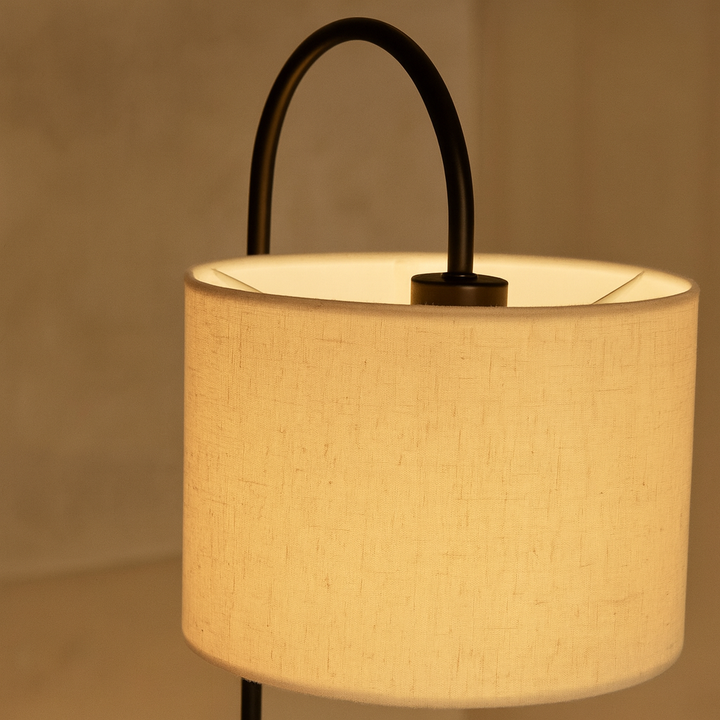 Close-up of a modern table lamp with curved black frame and glowing linen shade in a warm, softly lit room
