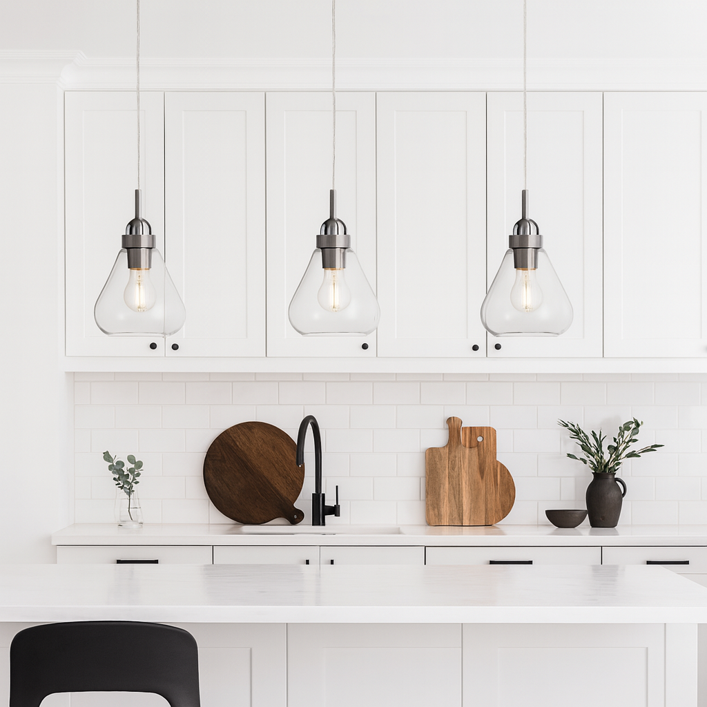 Clear glass pendant lights with brushed nickel detail above modern white kitchen island with black accents.