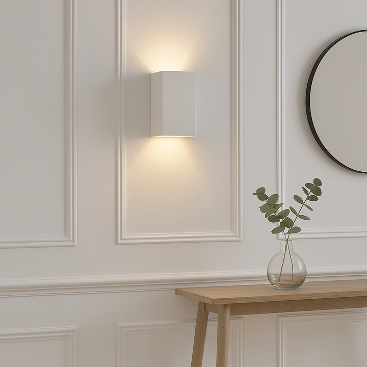Dover white ceramic wall light on white panelled hallway wall with warm glow, styled with console table, mirror, and glass vase with eucalyptus