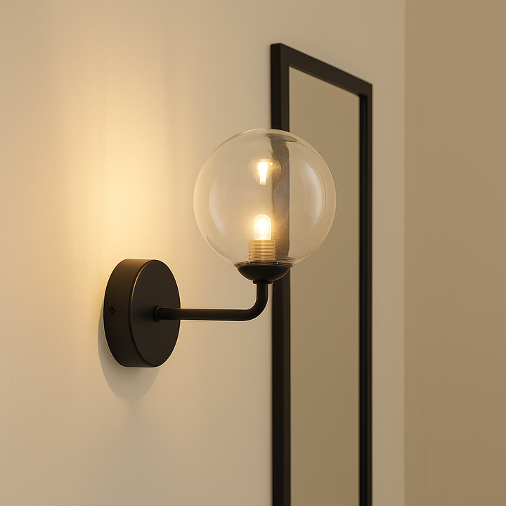 Fenland wall light with black frame and clear glass globe mounted on a cream wall, featuring warm glow G9 bulb