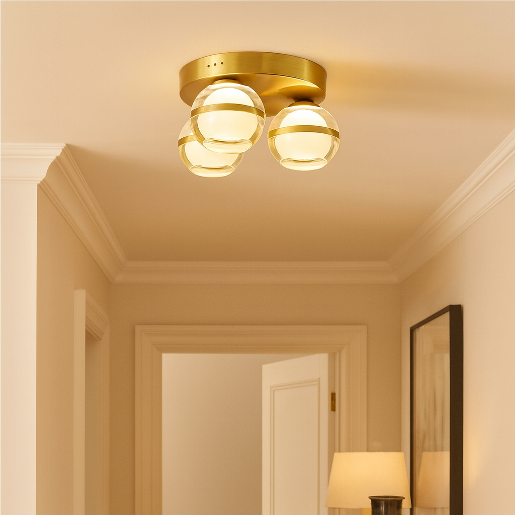 Small gold flush ceiling light with three glass globes styled in a warm neutral hallway interior.
