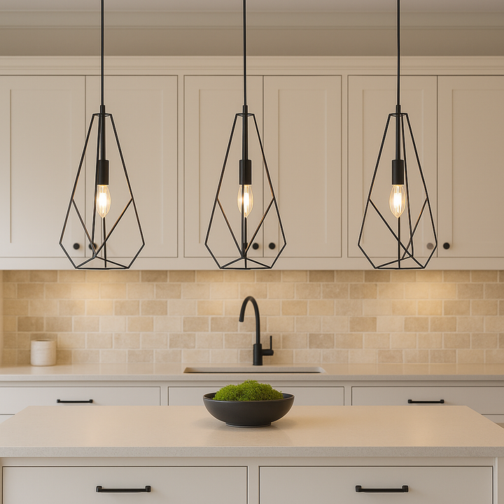 Three geometric black frame glass pendant lights hanging above a cream kitchen island with natural stone tile backsplash, black accents, and a black bowl filled with green moss.