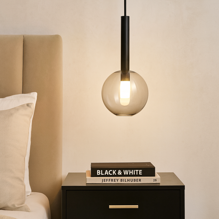 Modern bedroom with gold accents featuring a 20cm black pendant light with clear glass globe hanging over a black bedside table with stacked books.