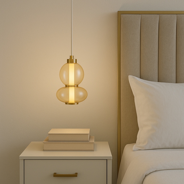 Modern bedroom with gold accents featuring a 20cm amber glass pendant light hanging over a cream bedside table with stacked realistic books.
