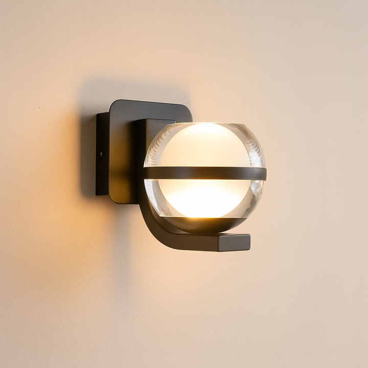 Alt text: Modern black wall light with clear glass globe casting a warm glow on a neutral wall