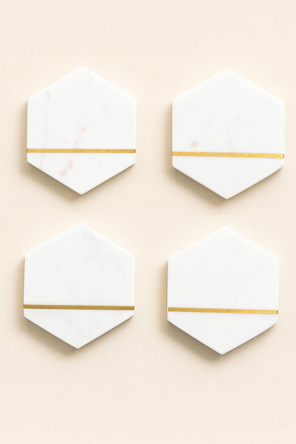 Flat lay of four white marble hexagon coasters with gold inlay, arranged in a square grid on a neutral background.
