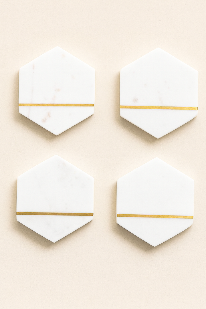 Flat lay of four white marble hexagon coasters with gold inlay, arranged in a square grid on a neutral background.