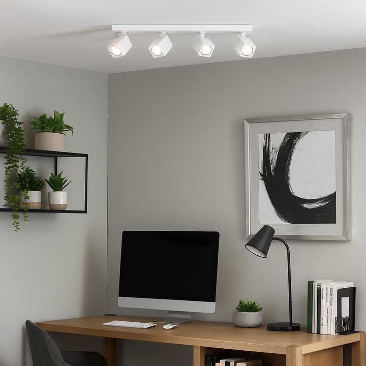 Wynyard White 4 Light Spotlight Bar mounted on the ceiling of a modern home office with wooden desk, computer, black desk lamp, plants, and abstract artwork.