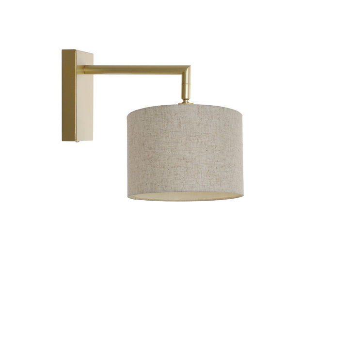 A gold wall light fixture with a beige fabric shade, mounted on a wall.