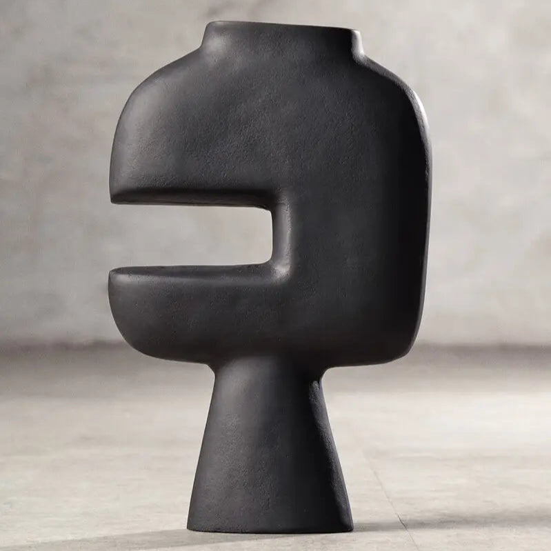 Black abstract vase on a light wooden floor with a neutral gray wall background