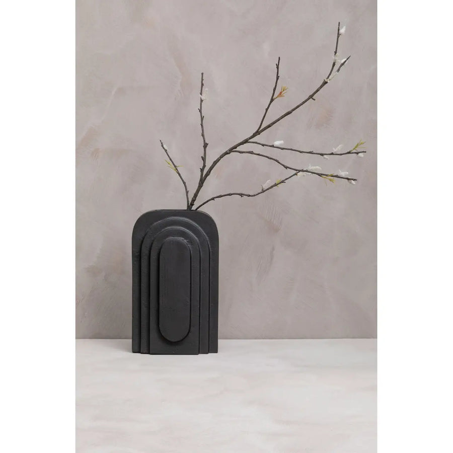 Black vase with a branch on a light gray background