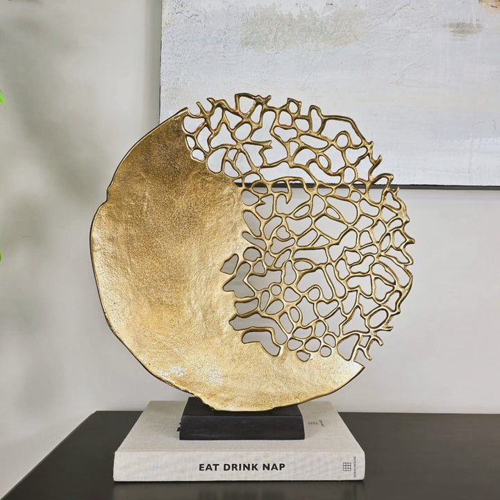 A champagne gold finish coral inspired sculpture with a black rectangular base, displayed on a table.