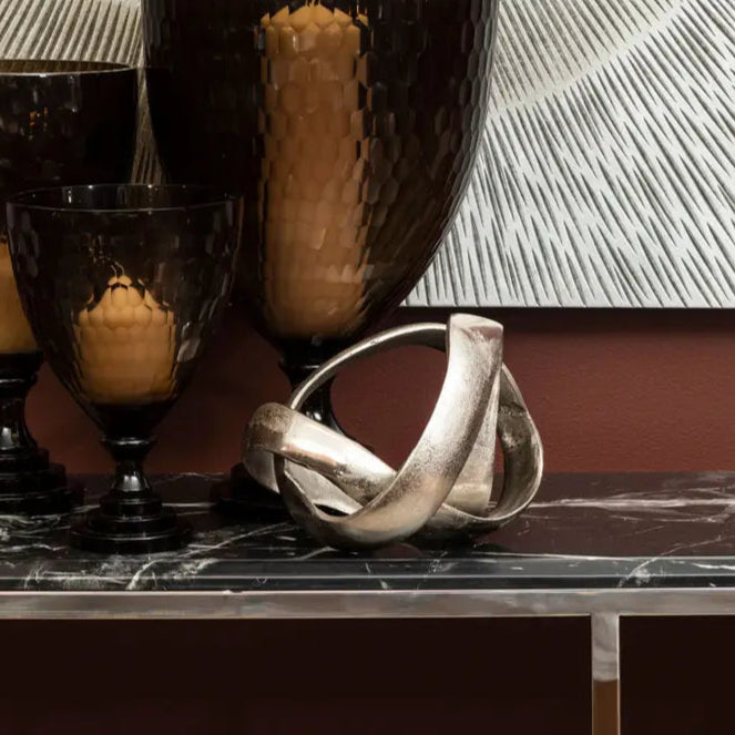 Decorative setting with dark glass containers and candles against a starburst patterned wall.
