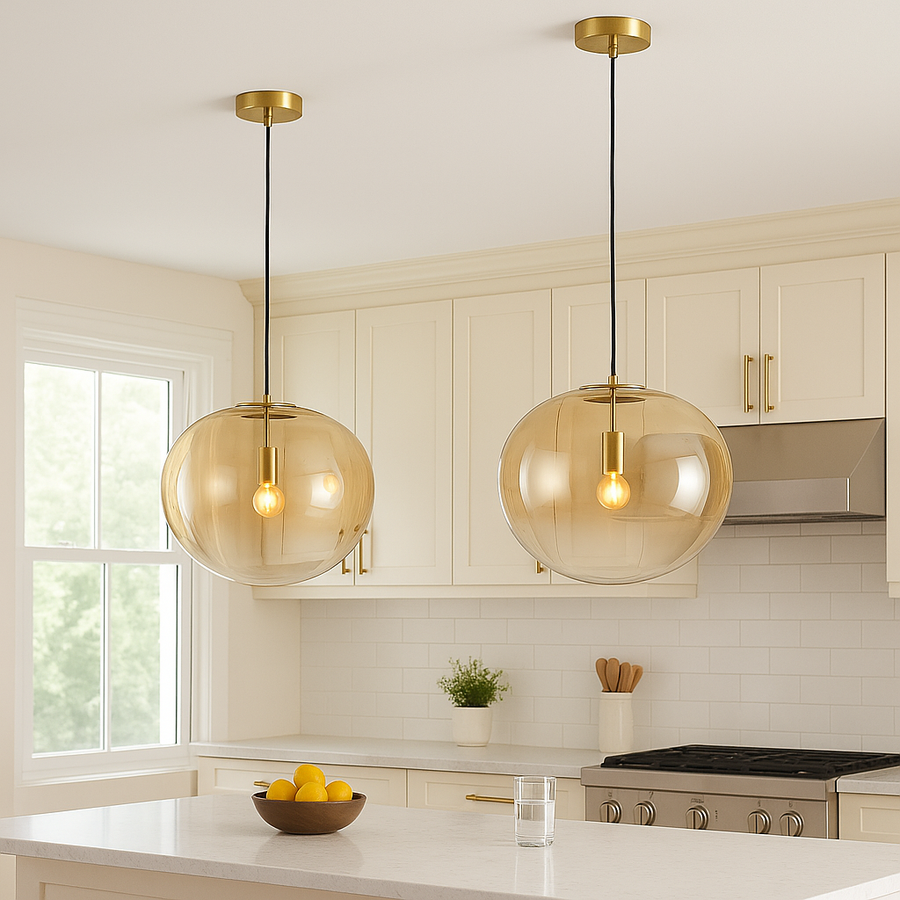 Two amber glass pendant lights with brass fittings hanging over a marble kitchen island with cream cupboards and brass handles