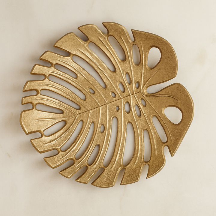 Overhead view of antique gold monstera leaf decorative dish with openwork design styled on light marble surface