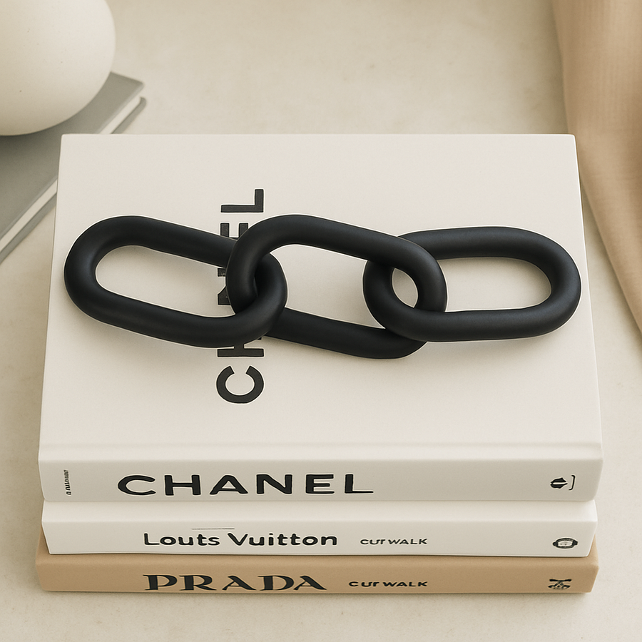 Luxury lifestyle image of a black chain link sculpture arranged in an S-shape on top of stacked designer coffee table books for modern home styling