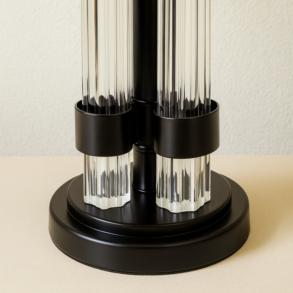 Close-up detail of black and glass column table lamp base resting on a light surface, showing fluted glass rods and matte black metal bands