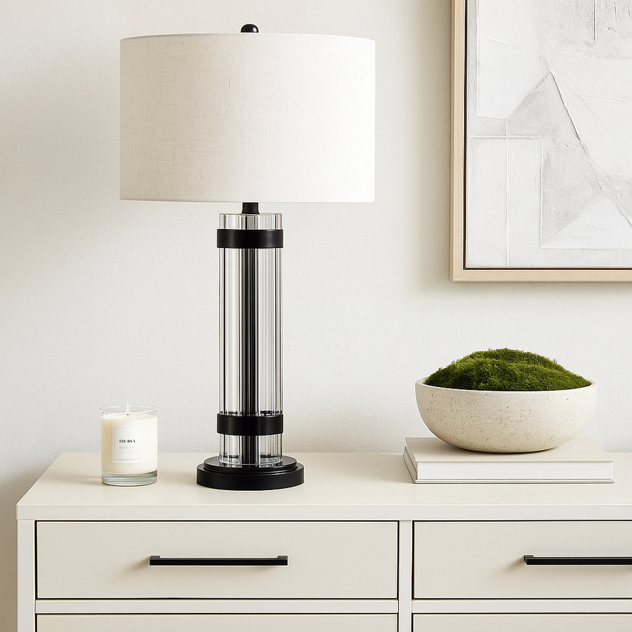 Luxury black and glass column table lamp with white fabric shade styled on a cream console with black handles and decorative moss bowl.