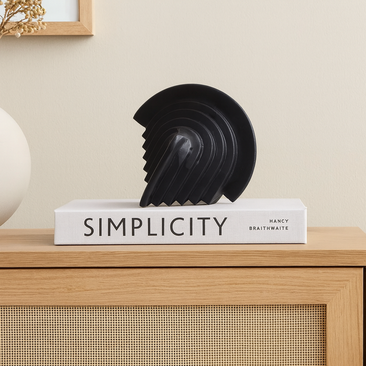 Black geometric sculpture styled on a Nordic media wall unit, placed on a modern coffee table book for a minimalist home décor look.