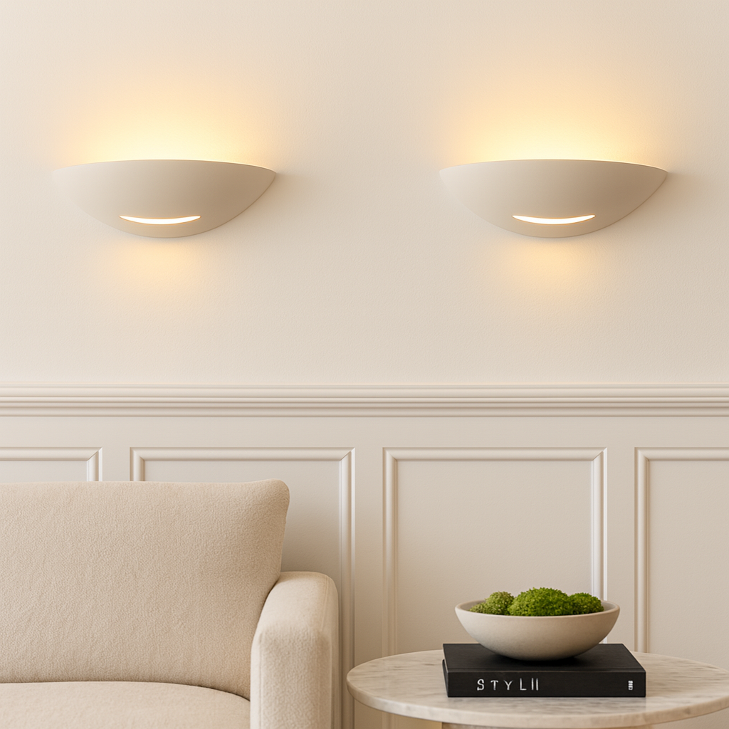 Pair of Brighton white ceramic wall lights with warm glow in a neutral living room with panelled walls, beige sofa and marble coffee table with moss bowl