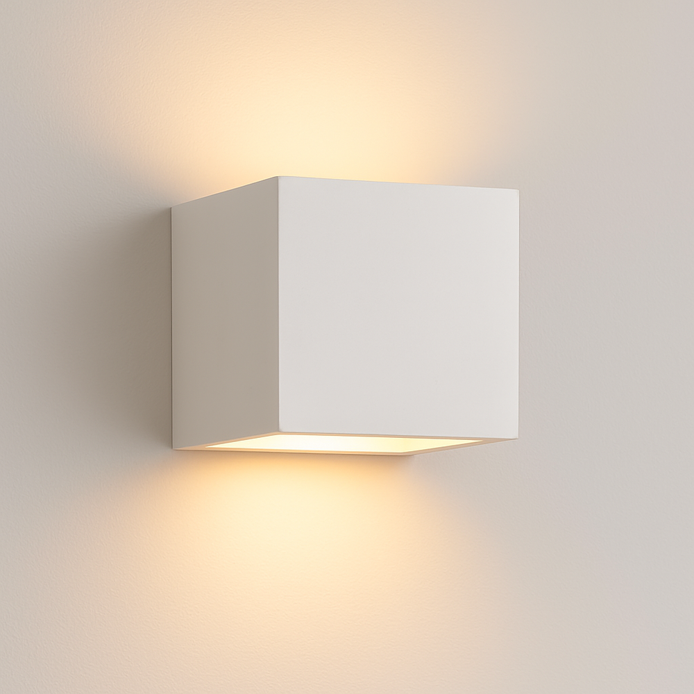 Cube-shaped ceramic wall light with smooth white finish and warm glow shining upwards and downwards on a clean white background