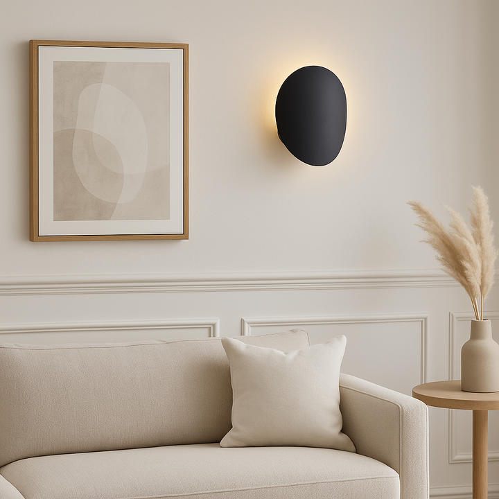 Delta black wall light in a modern living room with neutral sofa, artwork, and pampas vase.