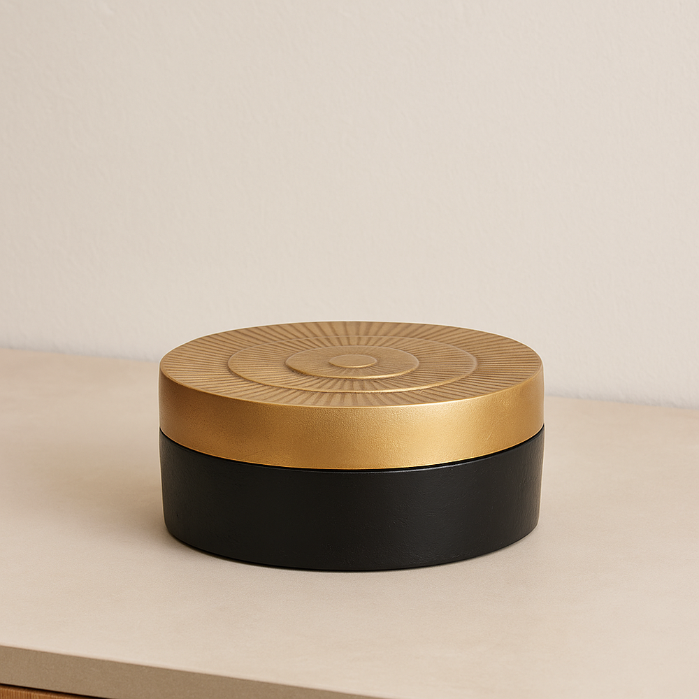 Round black and gold decorative trinket box with textured sunburst lid, styled on a light neutral surface in a modern home interior