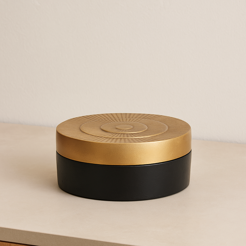 Round black and gold decorative trinket box with textured sunburst lid, styled on a light neutral surface in a modern home interior