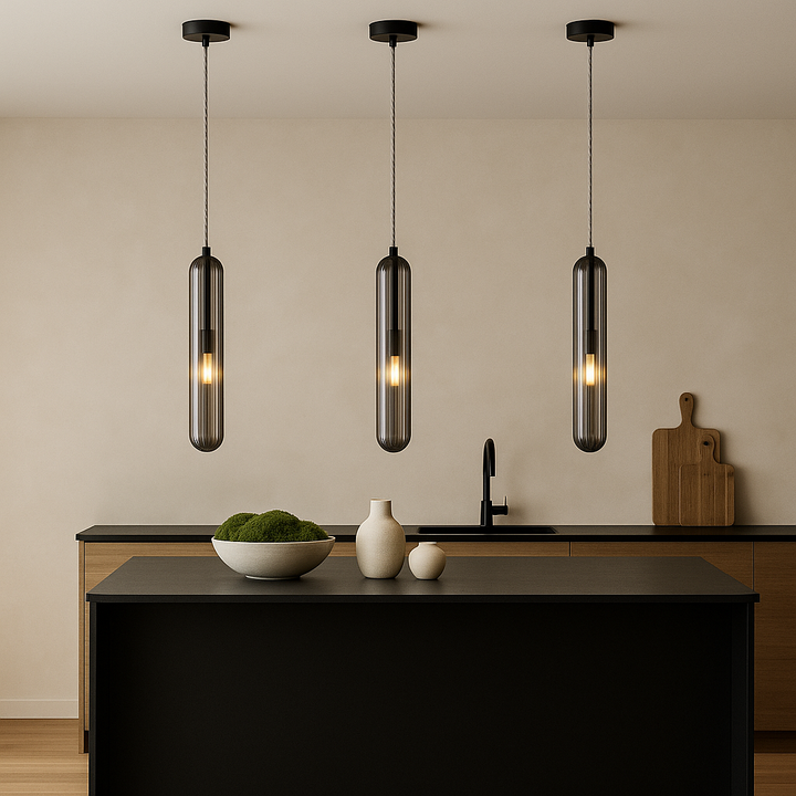 Set of three Florence smoked glass pendant lights hanging above a modern black kitchen island styled with a white bowl of green moss and minimalist vases
