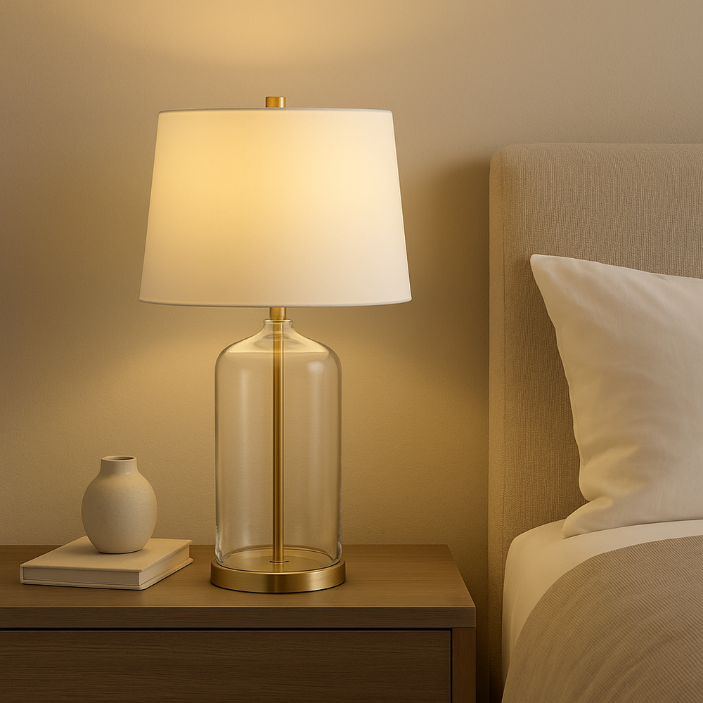 Luxury glass and gold table lamp with white shade styled on a wooden bedside table in a modern neutral bedroom
