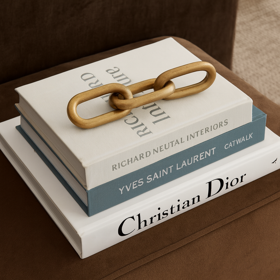 Luxury lifestyle image of a gold chain sculpture placed on top of stacked designer coffee table books, styled as a modern decorative book topper.