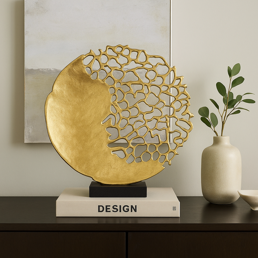 Luxury lifestyle image of a gold coral-inspired sculpture displayed on a dark wood console with a design book, artwork, and ceramic vase for modern home styling