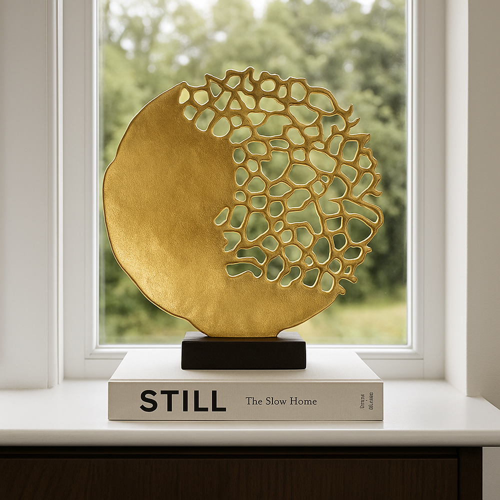 Luxury lifestyle image of a gold coral-inspired sculpture with a black base, displayed on a large styling book on a white windowsill
