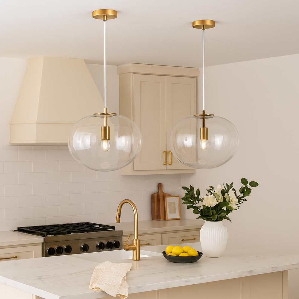 Pair of gold and clear glass pendant lights hanging over a cream kitchen island with marble top