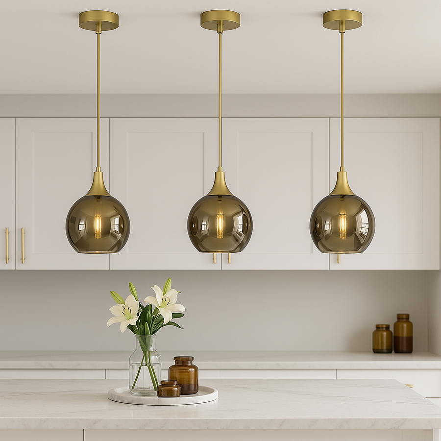 Three gold smoked glass pendant lights evenly spaced above a modern white kitchen island with gold accents.