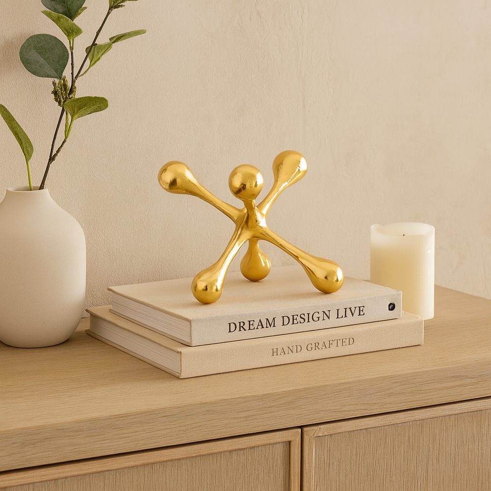 Luxury gold metal jack sculpture styled on books with vase and candle on a modern sideboard.
