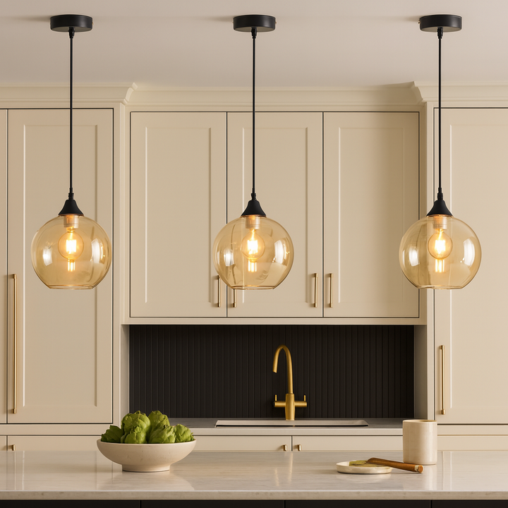 Luxury kitchen with three Irvine amber glass pendant lights hung above a marble island, featuring cream cabinets with black accents and gold details for a modern elegant look.