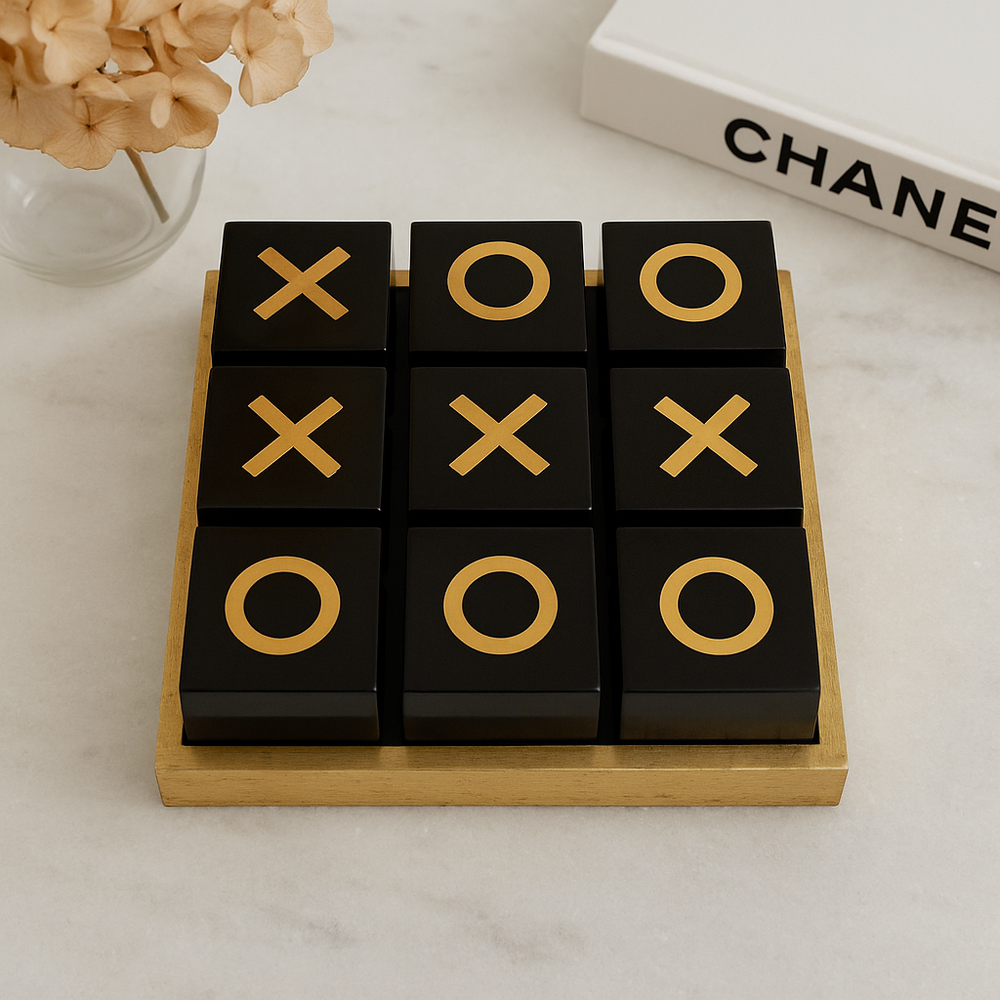 Luxury black and gold noughts and crosses set on marble table with vase and Chanel book