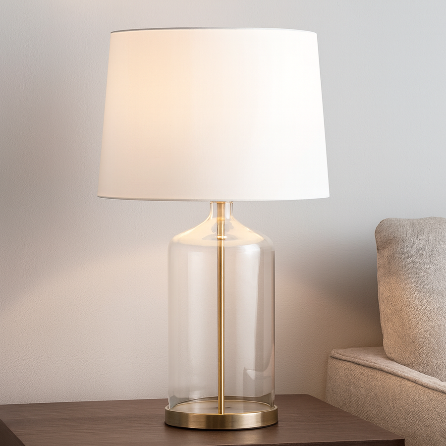 Luxury table lamp with clear glass base, gold detailing and white drum shade styled on dark wood side table in modern living room