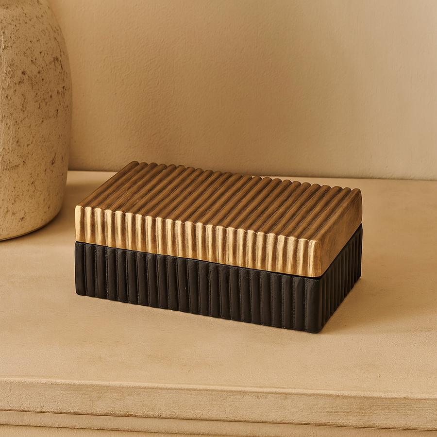 Luxury rectangular metal storage box with gold ridged lid and black grooved base styled on a sideboard in a modern home interior