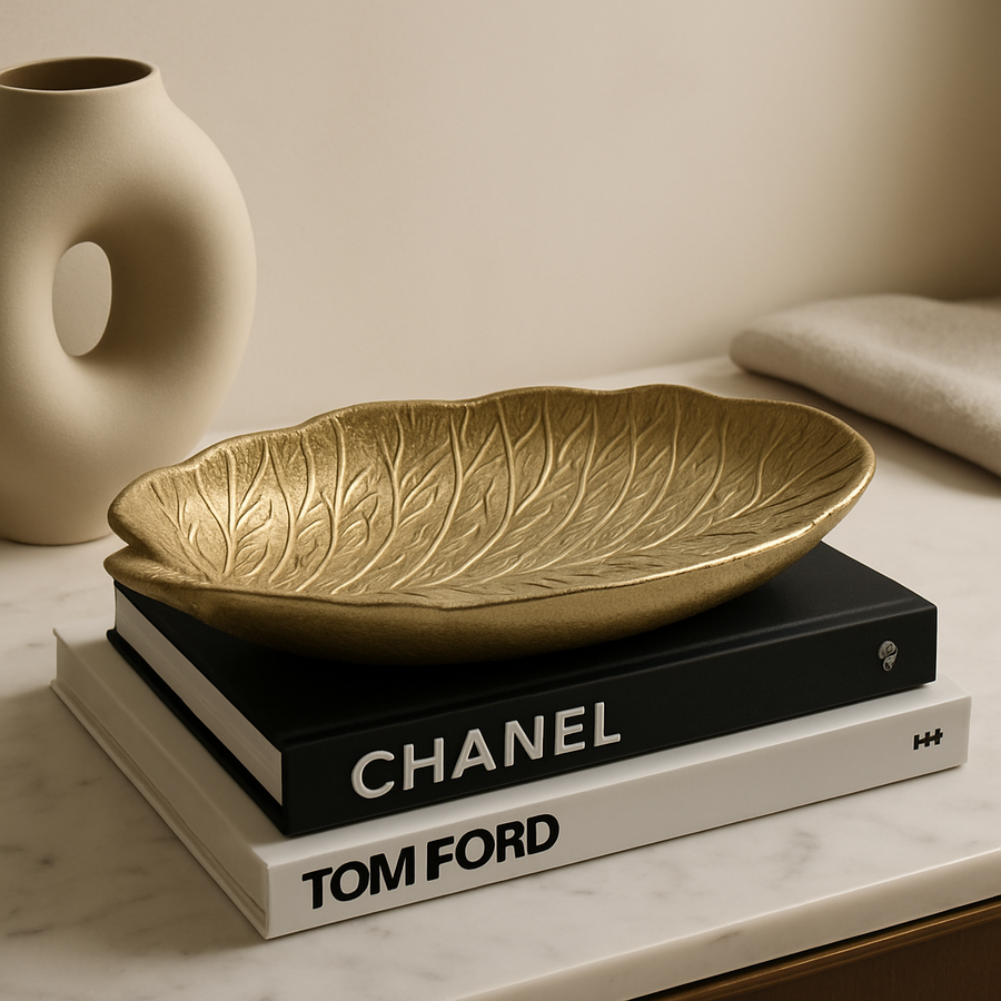 Luxury gold leaf-shaped decorative bowl styled on marble surface with designer books and modern neutral vase in a contemporary home interior