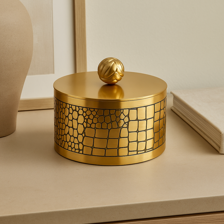 Luxury round gold metal trinket box with textured pattern and decorative lid, styled on a neutral sideboard in a modern home interior