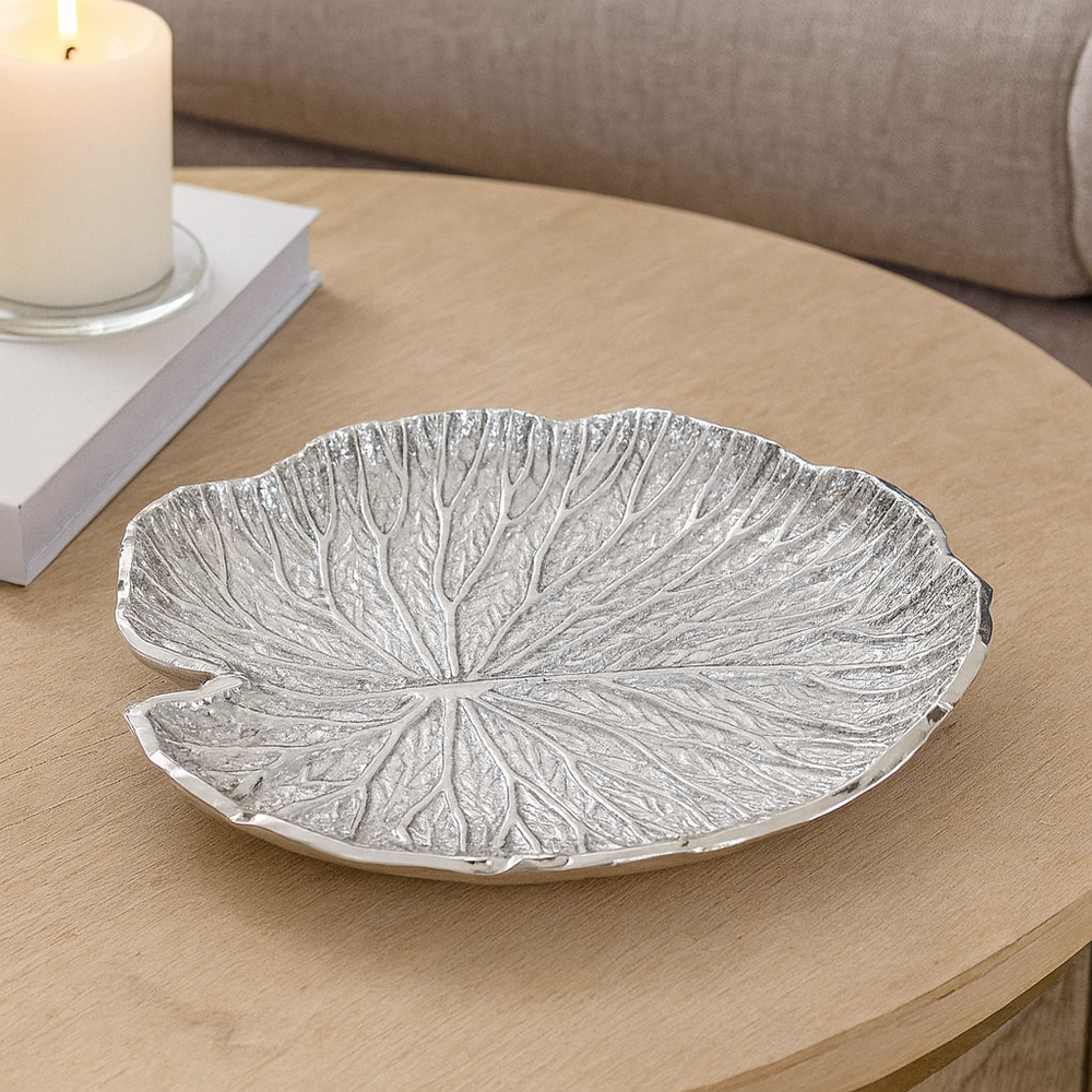 Luxury silver metal leaf bowl styled on a modern wooden table with candle in neutral home setting